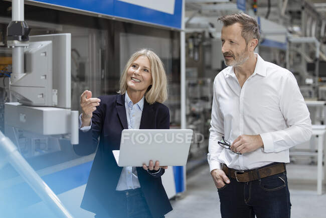Sourire geste professionnel féminin tout en discutant avec un collègue masculin sur les machines dans l'usine — Photo de stock