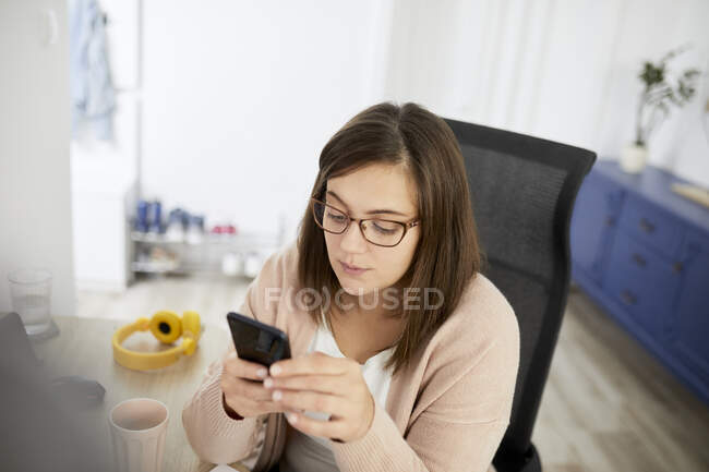 Femme pigiste utilisant un téléphone intelligent tout en travaillant à la maison — Photo de stock