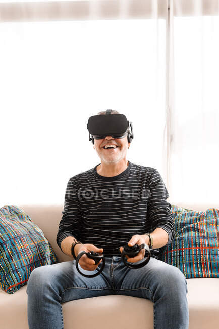 Счастливый зрелый мужчина играет с симулятором виртуальной реальности на диване дома — стоковое фото