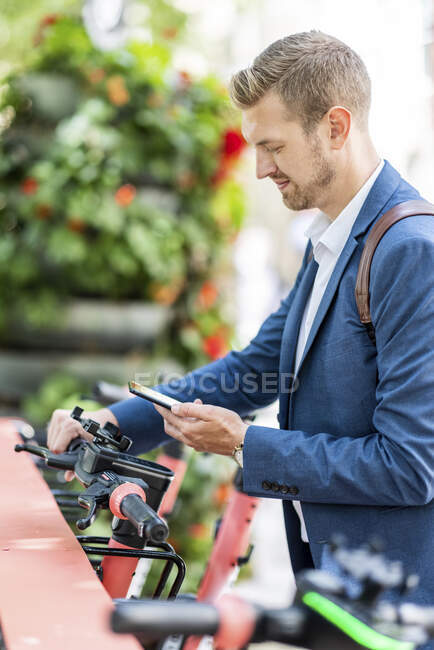 Masculino profissional desbloqueio elétrico empurrar scooter através do telefone móvel na estação de estacionamento — Fotografia de Stock