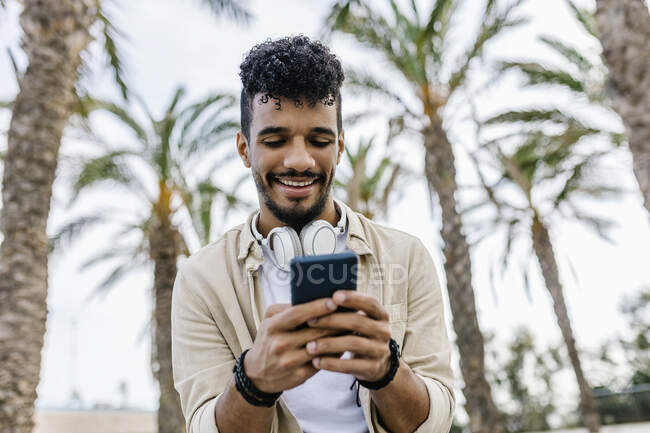 Smiling young man with black hair using smart phone — Stock Photo