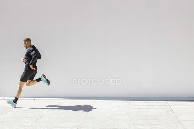 Joven atleta masculino corriendo por la pared blanca - foto de stock