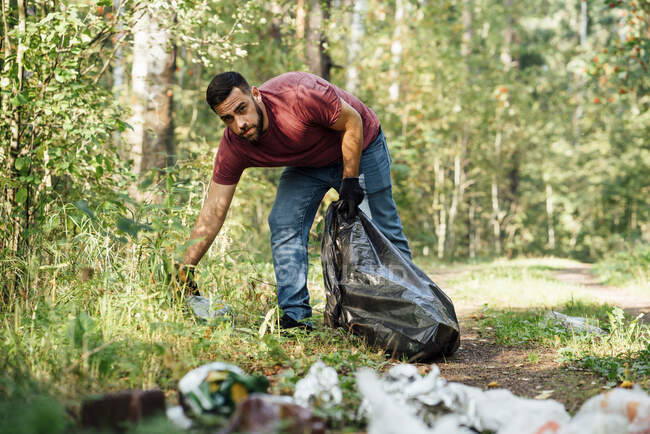 Mid adult male environmentalist putting plastic bottle in garbage bag — Stock Photo