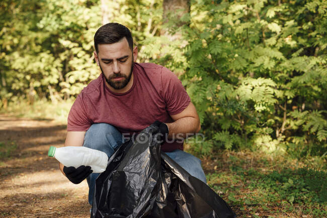 Voluntário masculino colocando garrafa de plástico no saco de lixo — Fotografia de Stock