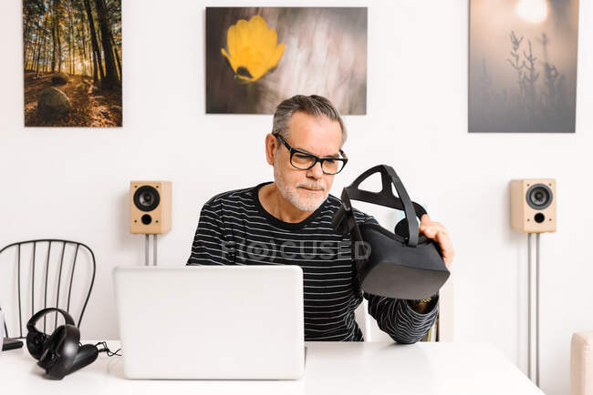 Mature man with laptop examining virtual reality simulator at home — Stock Photo