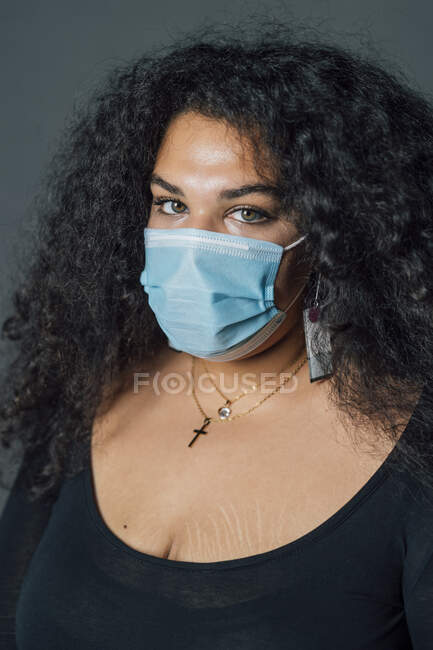Mujer con cabello rizado usando mascarilla protectora contra fondo gris - foto de stock