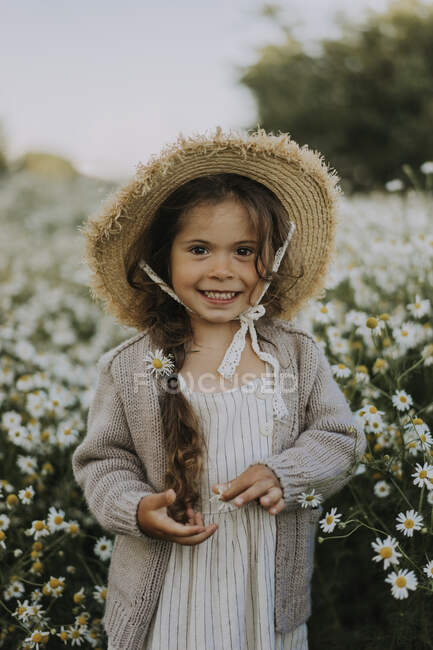 Chica sonriente con sombrero de pie en el campo de flores - foto de stock