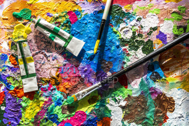 Tubes de peinture et pinceaux sur palette désordonnée — Photo de stock