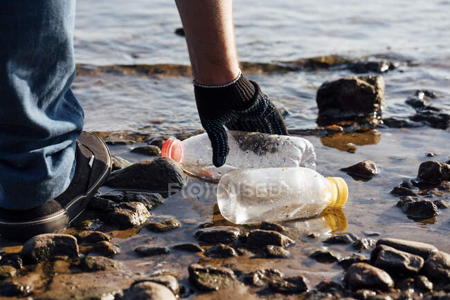 Мужчина-активист собирает пластиковые бутылки на берегу реки — стоковое фото