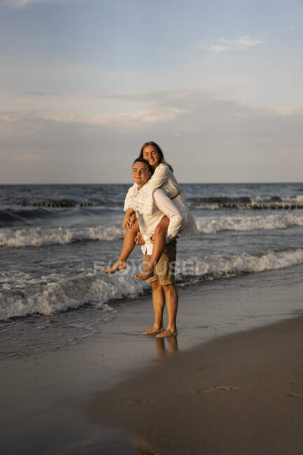 Fidanzato dando fidanzata cavalcata in spiaggia al tramonto — Foto stock