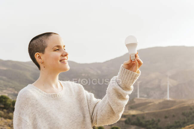Sorrindo raspada mulher cabeça segurando lâmpada no parque eólico — Fotografia de Stock
