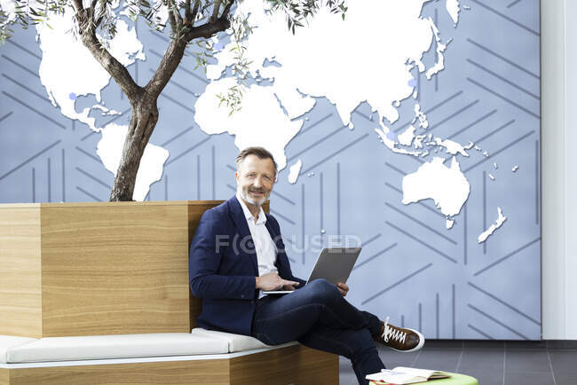 Homme souriant professionnel avec ordinateur portable assis sur le siège dans le bureau — Photo de stock