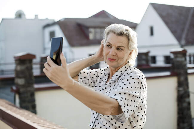 Senior woman taking selfie through smart phone on rooftop — Stock Photo