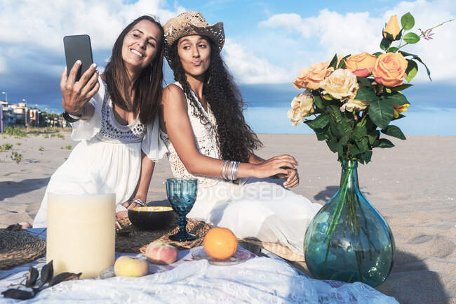 Mujer tomando selfie con una amiga a través de un teléfono inteligente en la playa - foto de stock