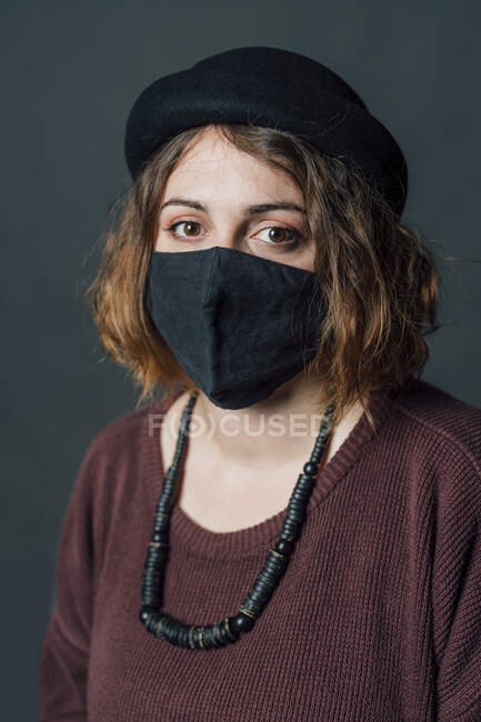 Donna con cappello indossando maschera protettiva contro sfondo grigio — Foto stock