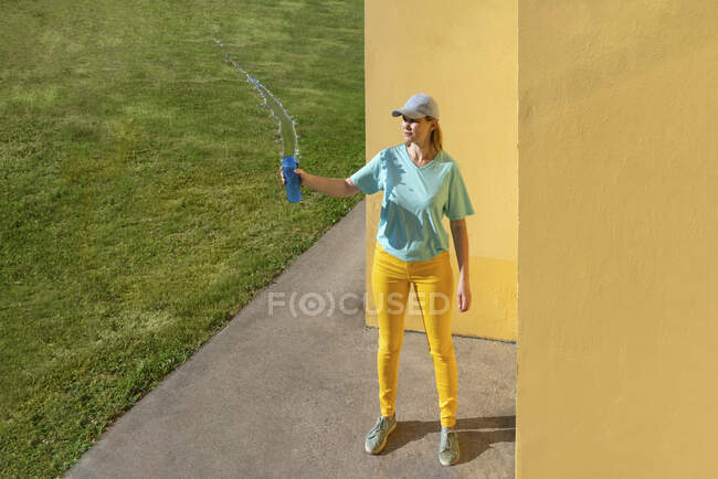 Woman throwing water while standing by yellow wall — Stock Photo