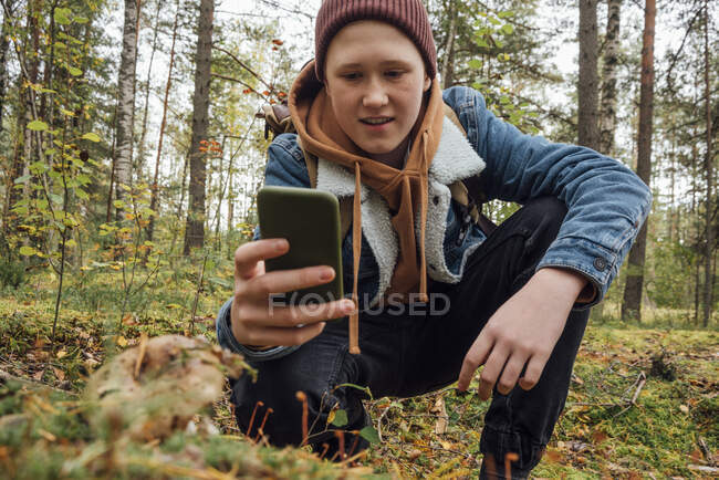 Garçon photographier par téléphone intelligent tout en s'agenouillant dans la forêt — Photo de stock
