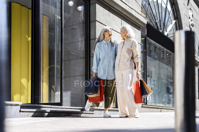 Друзья смотрят друг на друга, держа сумки возле магазина. — стоковое фото