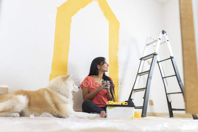 Smiling young woman having coffee by Akita dog at home — Stock Photo