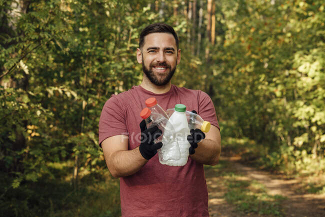 Мужчина-активист держит пластиковые бутылки в лесу — стоковое фото
