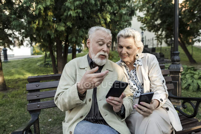 Coppia utilizzando smartphone mentre seduto sulla panchina — Foto stock