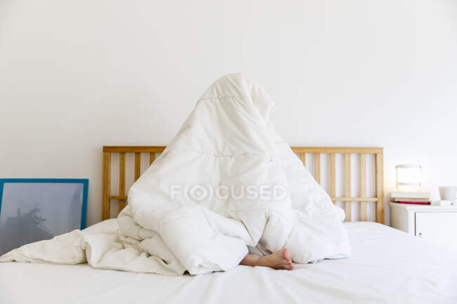 Jovem envolto em cobertor branco enquanto sentado na cama em casa — Fotografia de Stock