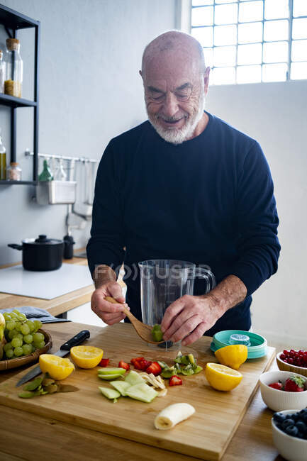 Uomo anziano che prepara frullato al bancone della cucina — Foto stock