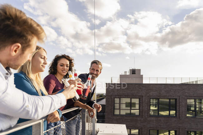 Collaboratori sorridenti brindare bottiglie in terrazza — Foto stock