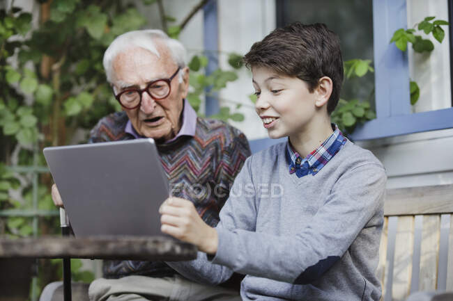 Garçon souriant montrant ordinateur portable à grand-père dans la cour arrière — Photo de stock