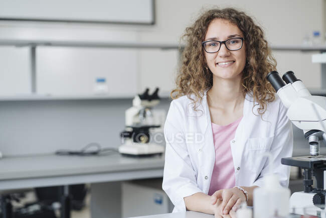 Jeune scientifique souriant au microscope au bureau du laboratoire — Photo de stock