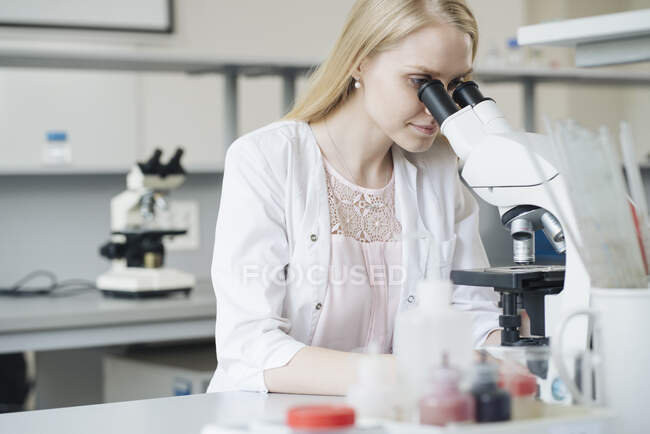 Cientista loira pesquisando através de microscópio em laboratório — Fotografia de Stock