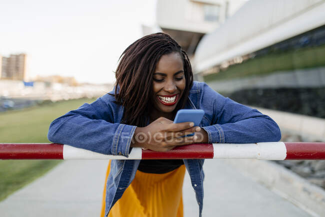Woman using smart phone leaning on pole — Stock Photo