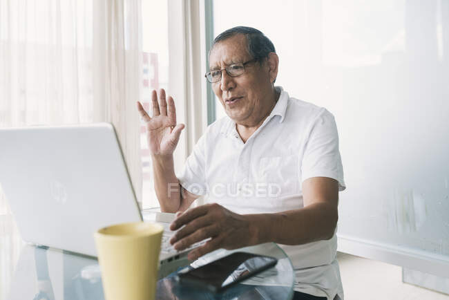 Uomo anziano che agita mano sulla videochiamata attraverso il computer portatile a casa — Foto stock
