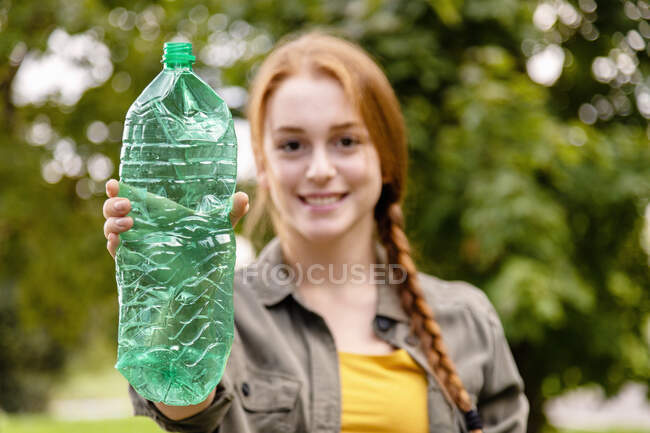 Ambientalista femenina sonriente mostrando botella de plástico en el jardín - foto de stock