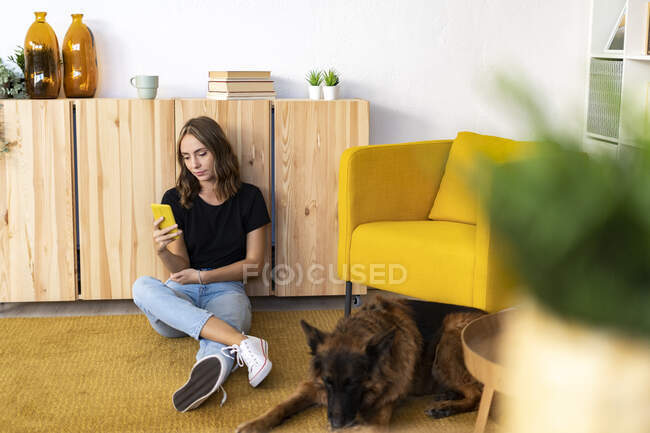 Giovane donna che utilizza lo smartphone di German Shepherd in salotto — Foto stock