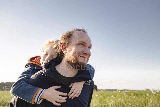 Sonriente hombre dando paseo a cuestas a su hijo - foto de stock