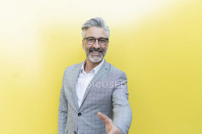 Felice uomo d'affari che fa stretta di mano davanti al muro giallo — Foto stock