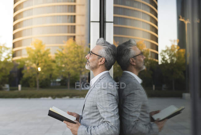 Homme d'affaires tenant livre appuyé sur le mur de verre — Photo de stock