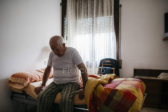 Самотній старший чоловік, що сидить удома на ліжку. — стокове фото