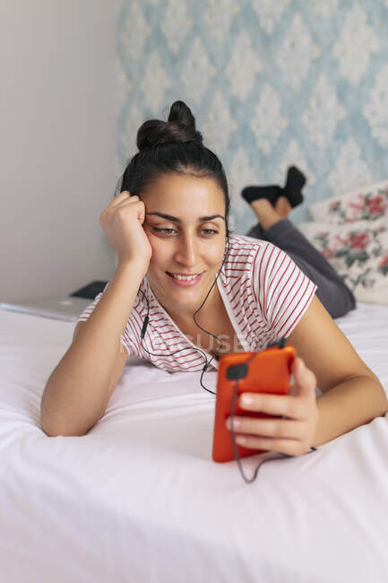 Donna sorridente utilizzando il telefono cellulare sul letto — Foto stock