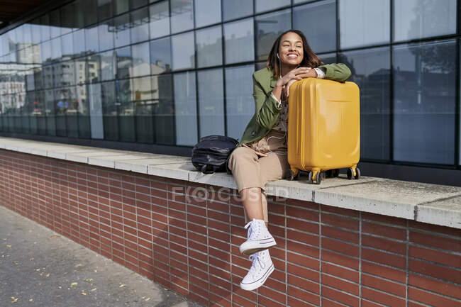 Smiling young woman leaning on luggage — Stock Photo