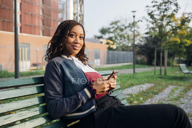 Улыбающаяся женщина с мобильным телефоном сидит на скамейке — стоковое фото