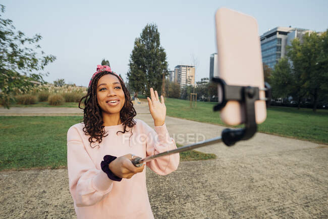 Mujer saludando la mano mientras vlogging a través del teléfono inteligente en el parque - foto de stock