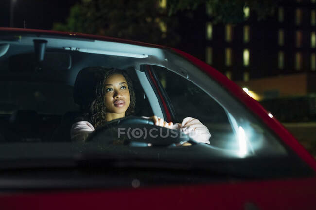 Jovem mulher dirigindo carro iluminado à noite — Fotografia de Stock