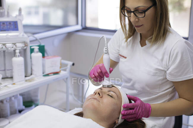Esteticista haciendo ultrasonido facial de mujer madura con equipo en salon - foto de stock