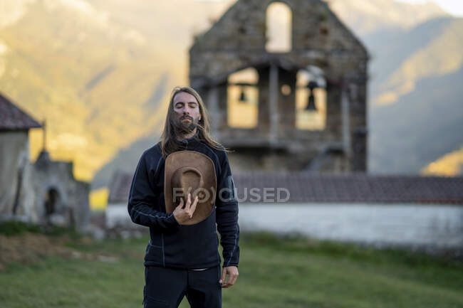 Uomo barbuto con gli occhi chiusi che tiene il cappello al cimitero — Foto stock