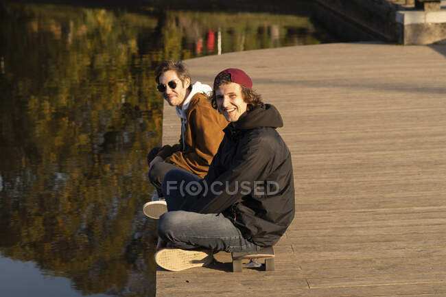 Smiling friends siting cross-legged on boardwalk — Stock Photo