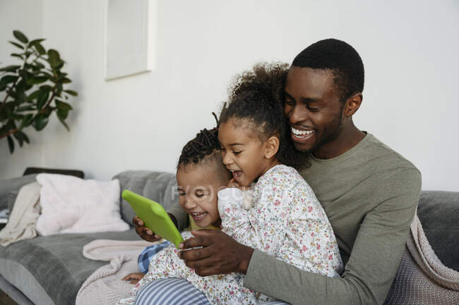 Веселые сын и дочь смотрят цифровой планшет с отцом на диване — стоковое фото