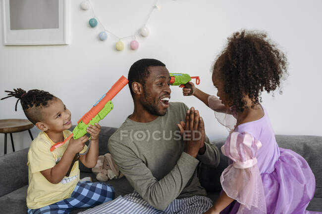 Дети с водяными пистолетами указывают на отца в гостиной. — стоковое фото