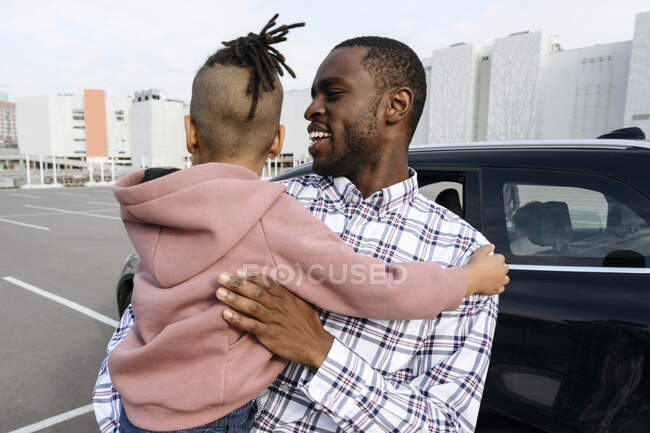 Sonriente padre llevando a su hijo en brazos en el estacionamiento - foto de stock